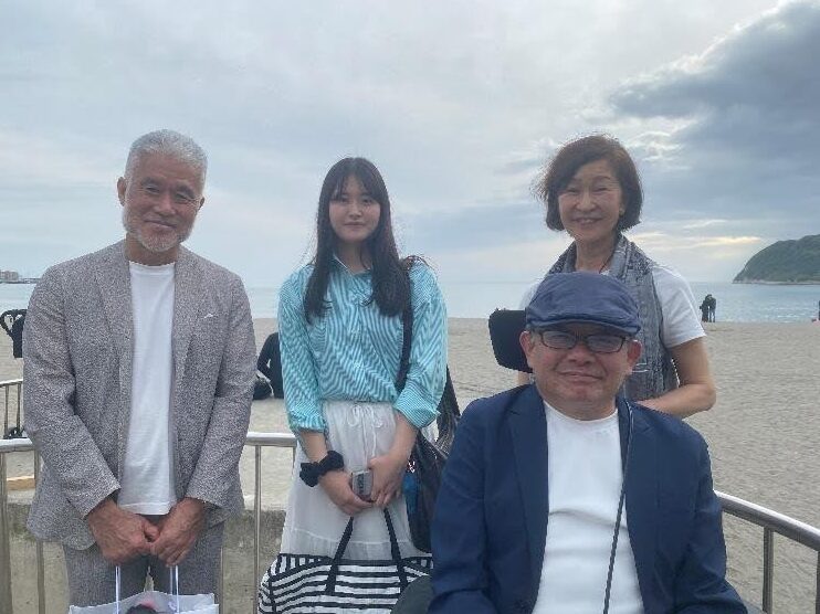 曇り空と海を背景に、4人が並んで立つ記念写真