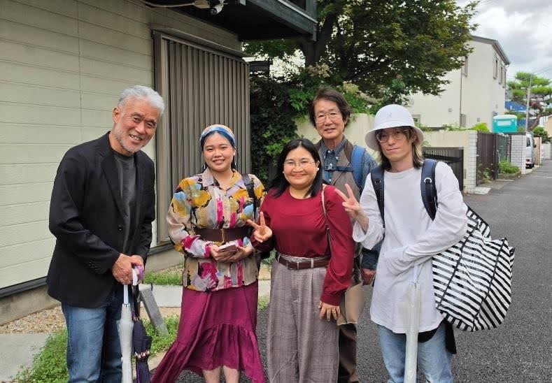 住宅街の路上で、カジュアルな服装の5人が笑顔で並ぶ集合写真。