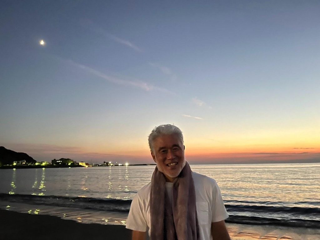 夕暮れの逗子海岸で、月と夕焼けを背に